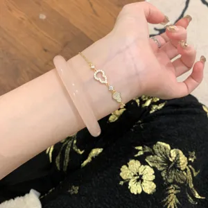 Primer plano detallado de una pulsera de calabaza brillante de circonio y un brazalete rosa en muñeca.