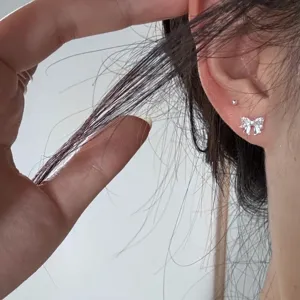 Gros plan de boucles d'oreilles nœud argentées portées à l'oreille, design minimaliste.