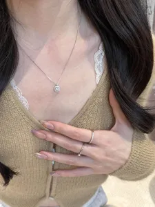 Collar de plata con colgante cuadrado en primer plano, cadena delicada con cristales brillantes.