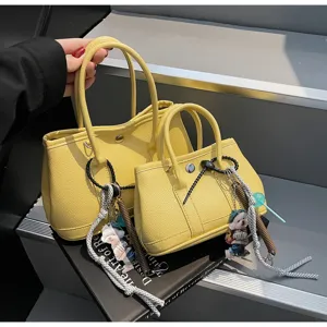 Detailansicht stilvoller gelber PU-Leder-Taschen in groß und klein mit süßen Anhängern.