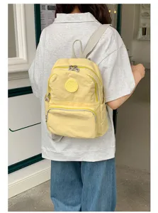 Vue de détail d'un sac à dos en tissu oxford jaune avec poches zippées et badge rond.