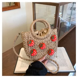Detailansicht der handgemachten Strohtasche mit niedlichen Plüsch Erdbeer Dekoren.