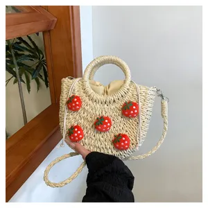 Nahtaufnahme der handgeflochtenen Strohtasche mit süßen Erdbeer-Anhängern und rundem Griff.