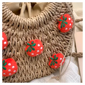 Nahaufnahme des geflochtenen Strohtaschen-Details mit süßen 3D-Erdbeer-Stickereien und Kordelzug.