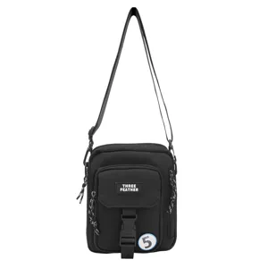 Detalle de bolso cruzado negro de lona con bolsillo delantero, cremallera y hebilla.