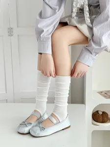Detailed shot of white stirrup leg warmers paired with silver ballet flats for women fashion.