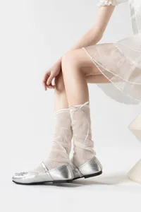 Detailopname van transparante beenwarmers met volant in balletstijl en zilveren schoenen.