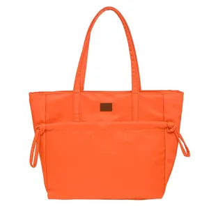 Primo piano della borsa tote in nylon arancione con dettagli del tessuto e toppa marrone.