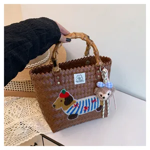 Dettaglio della borsa in paglia vintage con manico in bambù, ricamo di cane e ciondolo di peluche.
