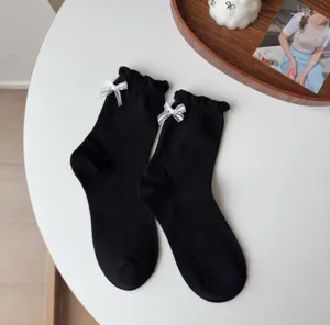 Nahaufnahme schwarzer Mittelsocken mit weißen Schleifen und niedlichen Rüschenrändern.