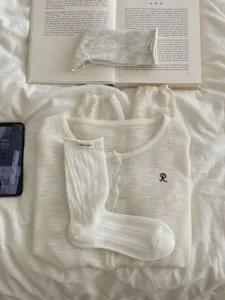 Detail shot of a Korean style white knitted cardigan and hollow socks flat lay on white bedding.