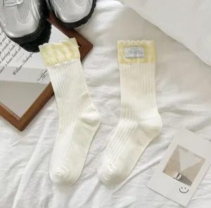 Detail shot of women white mid-tube socks featuring yellow checkered ruffle cuffs and cute label.