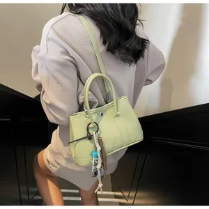 Detailansicht einer hellgrünen Ledertasche mit Schultergurt und stilvollen Anhängern.