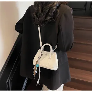 Detailansicht einer stilvollen weißen Mini-Umhängetasche mit eleganten Henkeln und Anhänger.