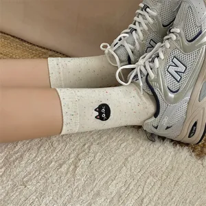 Close-up detail of cute cat embroidered cotton socks with speckled yarn design worn indoors.
