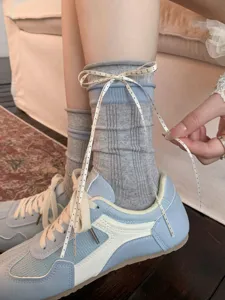 Detail shot of grey ribbed mid-calf socks featuring a cute polka dot ribbon bow and casual sneakers.