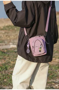 Detalle de bolso cruzado morado para exteriores con bolsillo con cremallera y lindo dije.