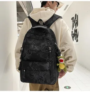 Detail view of black nylon campus backpack with letter print and cute dinosaur plush pendant.