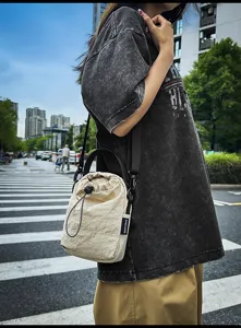 Detailed view of the casual beige drawstring bucket bag worn in urban street style.