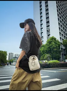 Casual street style outdoor shot showing the minimalist beige drawstring bucket bag in use.