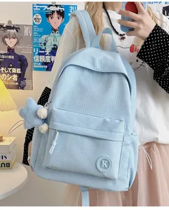 Close-up detail of the light blue plaid school backpack showing front pocket, patch logo and zipper.