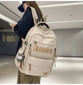 Detail view of the student plaid backpack with letter print and cute pendant in indoor setting.