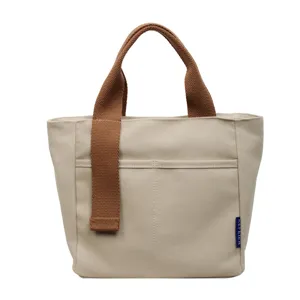Dettaglio di borsa a secchiello in tela con corpo beige, manici marroni e tasca frontale.