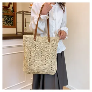 Vista dettagliata della borsa tote in paglia intrecciata con manici in pelle marrone.