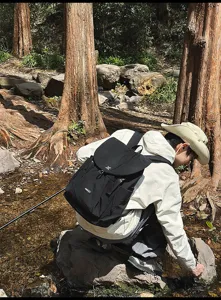 Vue extérieure détaillée d'un sac à dos noir près d'un ruisseau en forêt, design robuste.