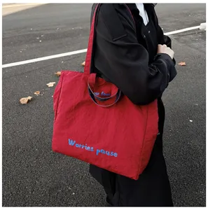 Primo piano dettaglio della borsa tote rossa casual con stampa di lettere blu per uso quotidiano.