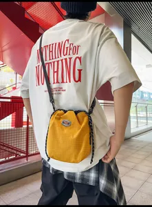 Detail shot of the yellow nylon drawstring bucket bag worn casually, showing its grid texture.
