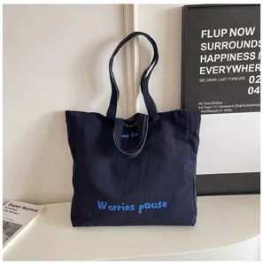 Dettaglio della borsa shopper in tela blu scuro con manici robusti e stampa di testo elegante.