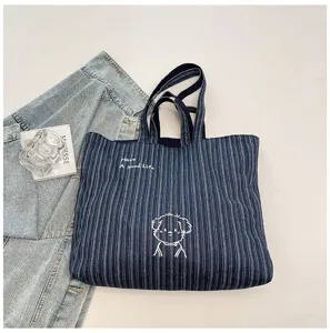 Vista dettagliata della borsa tote in denim a righe blu, con ricamo di cane e bella consistenza.