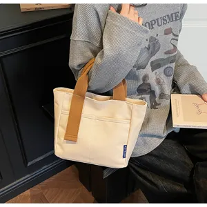 Vista dettagliata della borsa in tela casual con manici marroni e tasca frontale pratica.