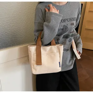 Borsa tote minimalista in tela con manici marroni a contrasto e tasca frontale per uso quotidiano.