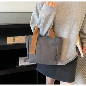 Borsa tote grigia in tela con manici marroni e pratiche tasche anteriori per gli spostamenti.