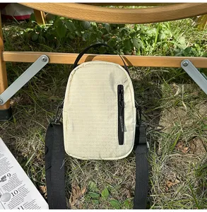 Detail shot of grid mini crossbody bag on outdoor grass with zipper pocket and strap.