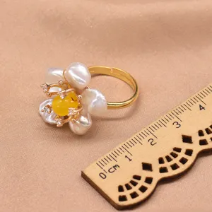 Primo piano dettagliato dell'anello fiore in perla barocca con pietra centrale gialla.