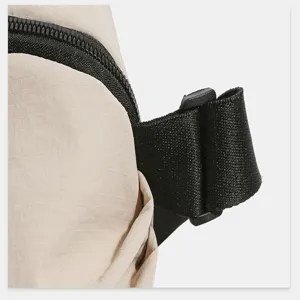 Close-up detail of khaki nylon chest bag zipper and adjustable black strap buckle.