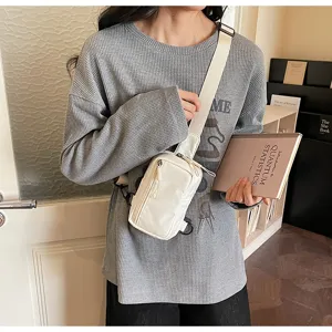 Detail shot of white crossbody chest bag worn by model, showing zipper pocket and durable strap.
