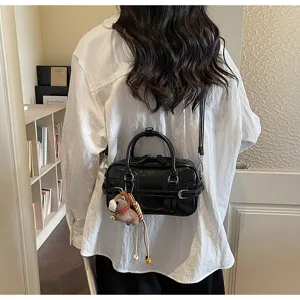 Detail view of the glossy PU black shoulder crossbody bag with cute plush charm and handle.