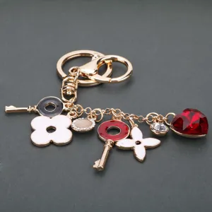 Elegante portachiavi in metallo dorato con trifoglio monogramma bianco e ciondolo cuore rosso.