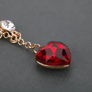 Primo piano dettaglio di un ciondolo in cristallo cuore rosso scintillante con catena.
