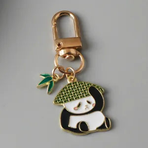 Close-up of a cute panda enamel keychain with a straw hat and green leaf charm