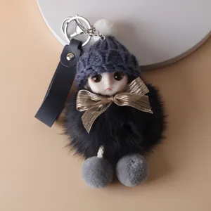 Close-up of a cute plush doll keychain with a blue knitted hat, bow, and soft black fur