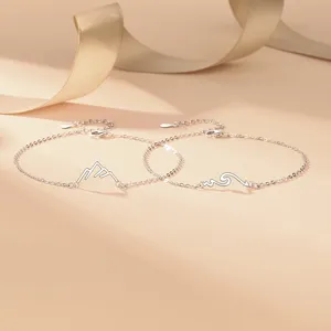 Close-up detail shot of couple silver bracelets with mountain and wave pendants on beige.