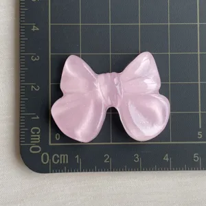 Dettaglio charm fiocco in resina glitterata traslucida rosa, finitura lucida per custodia telefono.