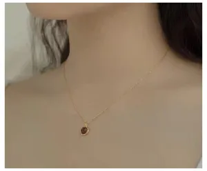 Primer plano detallado de un collar de plata delicado con un colgante de piedra roja.