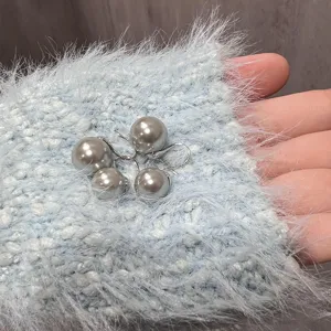 Close-up detail of grey pearl drop earrings with silver hook on blue fluffy fabric.