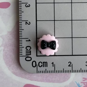 Detailed view of miniature black and pink resin bow charm for phone case DIY craft.